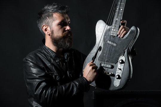 Stylish portrait of bearded men in black jacket with acoustic guitar. bearded man breaks a string on a guitar. Black background. an with long beard and mustache. Biker. Leather jacket