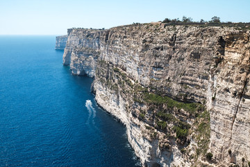 Fototapeta na wymiar a boat swimming at Ta Cenc Cliff at Sannat, Gozo island, Malta - walls of the giants