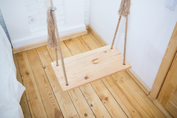 Wooden swing  with rustic ropes in the room loft interior. White apartment with bricks walls.