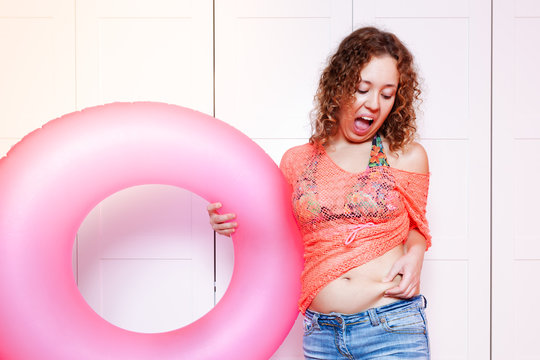Woman point to her belly and hold an inflatable round. Preparing for the vacation, diet concept, unready for vacation