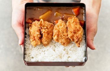 A female uses hands to holding and handing a dish of  Japanese curry rice topping with fried chicken and vegetables. Top view