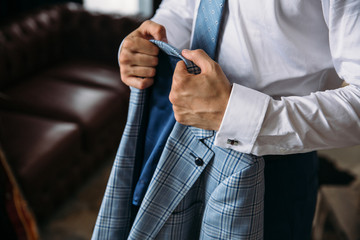 Close-up businessman groom wearing his blue checkered jacket at the morning of wedding day. Concept of men stylish elegance clothes.