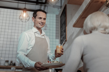 Enjoy your dinner. Pleased worker keeping smile on his face while giving healthy food to mature female