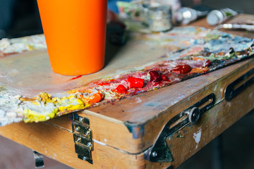 the palette with paints and a brush and is going to paint on canvas. to mix oil paints