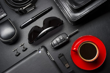 Man accessories in business style with cup of coffee, gadgets, car key, cufflinks, sunglasses, briefcase and other luxury businessman attributes on leather black background, fashion industry 