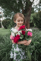 Portrait of smiling beautiful teenage with bouquet of daisies, against green of summer park.