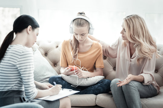 Behavior patterns. Anxious distressed mother consulting with female psychologist and teen girl listening to music