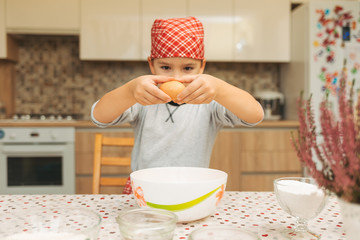 Little boy cooking. Child breaking egg into bowl. 