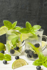 Summer refreshing drinks lemonade or cocktail Mojito with lime fresh mint blueberry ice. Light table, Dark wall Copy space
