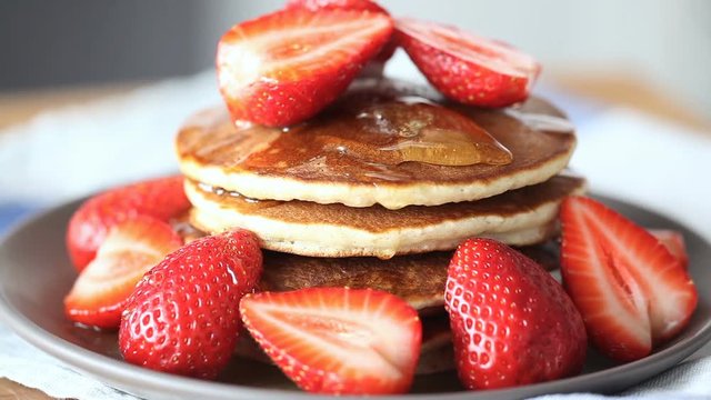 Closeup dripping honey. Honey dripping down a pancake stack and strawberry. Healthy breakfast.