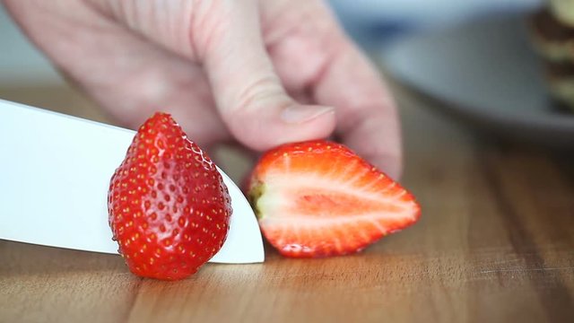 A female hands cutting strawberry on a wooden board. Strawberry slicing. Large knife cut the strawberry into two slices