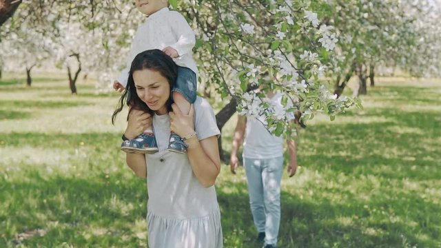 Smiling parents holding up cute son in summer apple tree park. Happy family concept. Young family have fun outdoors in slow motion with copyspace