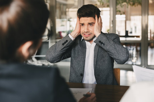Nervous uptight male candidate 30s worrying and grabbing his head during job interview in office, with group of managers - business, career and recruitment concept