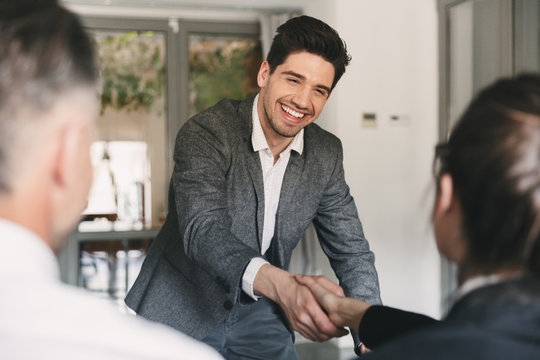 Business, career and placement concept - happy european man wearing suit rejoicing and shaking hands with group of employee, when was recruited during interview in office