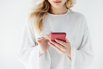 cropped shot of woman in white clothing using smartphone on grey backdrop