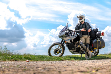 Rider Man and off road adventure motorcycles with side bags and equipment for long road trip, river and clouds on background, enduro travel touring concept