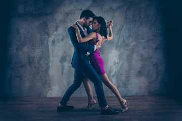 Full size body portrait of lovely attractive couple standing close in tango position face to face dancing, charming lady in purple tight dress gentlemen in tux isolated on grey background movement - obrazy, fototapety, plakaty