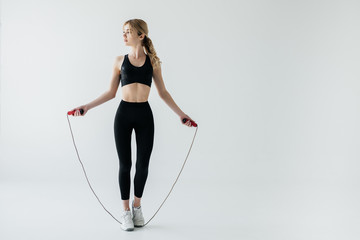 young sportive woman with skipping rope isolated on grey - obrazy, fototapety, plakaty