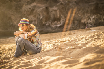 pretty blonde young woman sit down on the sand at the beach relaxing and enjoying sunset and sunny day of vacation. stay well in a natural place and outdoor leisure activity concept. colored clothes