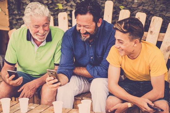complete family caucasian people men sitting on a wood bench looking smartphones. grandfather father and son all together enjoying the leisure outdoor time with smile and fun. technology 