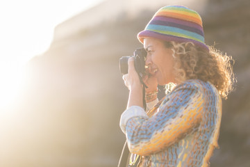 woman caucasian photographer with nice coloured hat taking pictures with old little camera. sunlight and sun flare in the background. bright summer concept image of nice people active taking memories