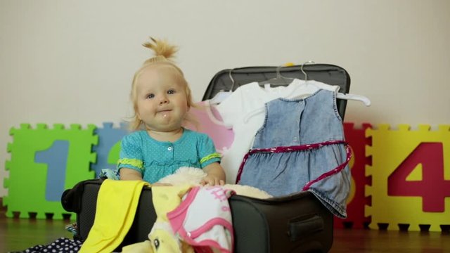 A small child is sitting in a suitcase with clothes. Travel and family tourism.