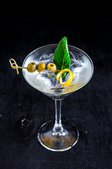 Cool transparent cocktail with olives on black background