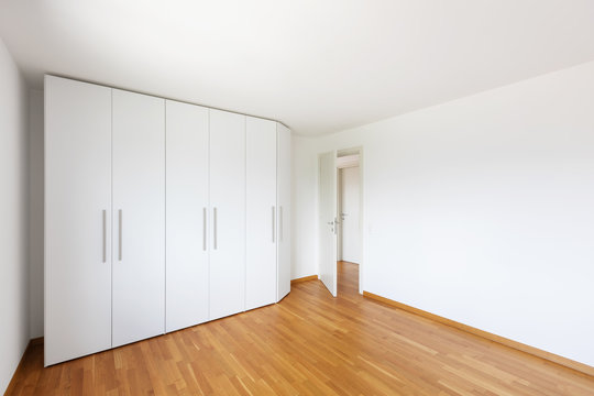 White empty room with large white wardrobe and open door on the corridor
