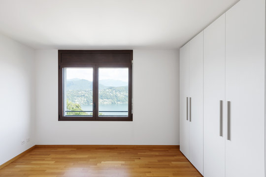 White empty room with windows overlooking the lake and large white wardrobe