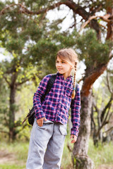 Little girl with backpack traveling in the forest