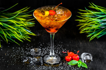 Sweet orange cocktail with cherry and ice on black background