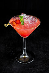 Pink cocktail with cherry and ice on black background