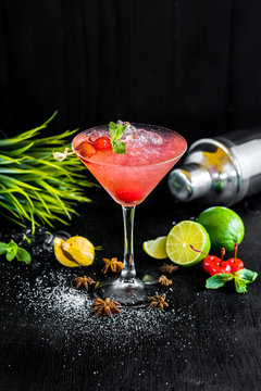 Pink cocktail with cherry and ice on black background