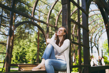 Portrait of beautiful caucasian young woman with charming smile wearing light casual clothes. Smiling female sitting under archway in city park in street outdoors on spring nature. Lifestyle concept.