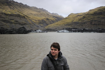 Young male tourist posing in front of mountains and icebergs in the background, photo taken in Iceland
