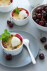 Cherry crumble with oatmeal and ice cream in bowl on grey wooden desk. Summer healthy food
