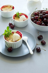 Cherry crumble with oatmeal and ice cream in bowl on grey wooden desk. Summer healthy food