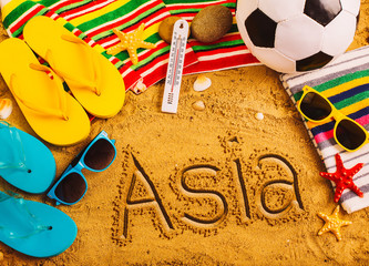 Summer concept of sandy beach, colorful flip flop shoes, sunglasses, ball and inscription asia