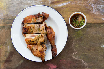 Top view of grilled chicken in white plate and sauce on wood background with copy space