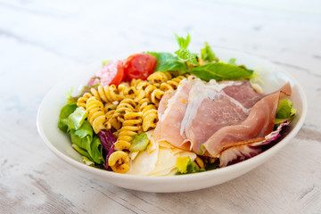 Salad with fusilli pasta accompanied tomatoes, mozzarella, smoked ham and italian cheese
