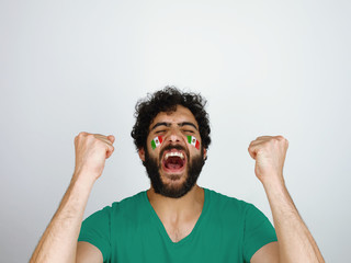 Sport fan screaming celebrating the triumph of his team. Man with the flag of Mexico makeup on his face and red t-shirt.                