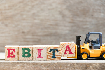 Toy forklift hold letter block A in word EBITA (abbreviation of  earnings before interest, taxes and amortization) on wood background