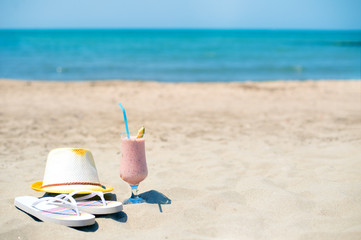 Strawberry fresh smoothie juice, hat and slippers near sea on sandy beach