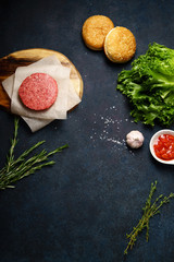 Cooking burger: classical american burger ingredients on dark blue background with copy space. Raw beef patties, vegetables, buns, lettuce.