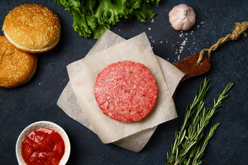 Cooking burger: classical american burger ingredients on dark blue background with copy space. Raw beef patties, vegetables, buns, lettuce.