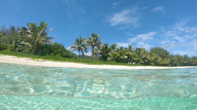 SLOW MOTION, HALF UNDERWATER: Popular white sand beach on remote tropical island is left empty during the tourist low season despite the stunning view of the glassy ocean water and lush palm trees.