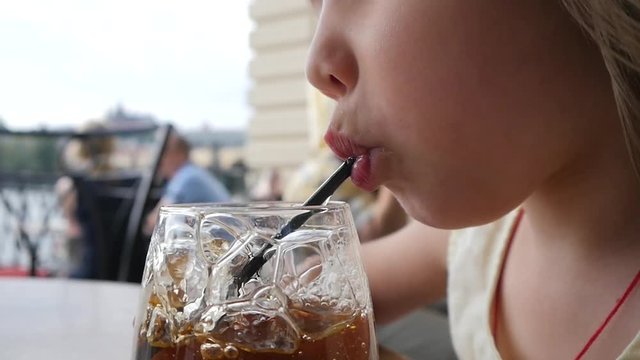 Funny little child girl portrait enjoy making bubbles in glass of juice with straw at street restaurant table