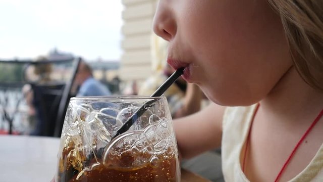 Funny little child girl portrait enjoy making bubbles in glass of juice with straw at street restaurant table