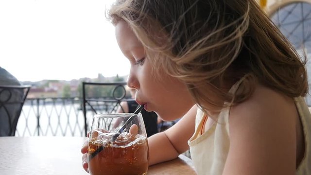 Funny little child girl portrait enjoy making bubbles in glass of juice with straw at street restaurant table