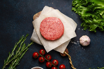 Cooking burger: classical american burger ingredients on dark blue background with copy space. Raw beef patties, vegetables, buns, lettuce.